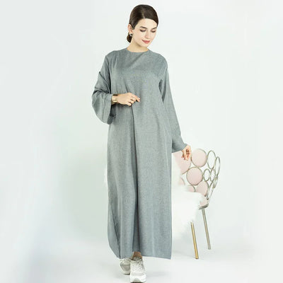 Woman wearing a loose grey maxi dress with long sleeves and white sneakers indoors